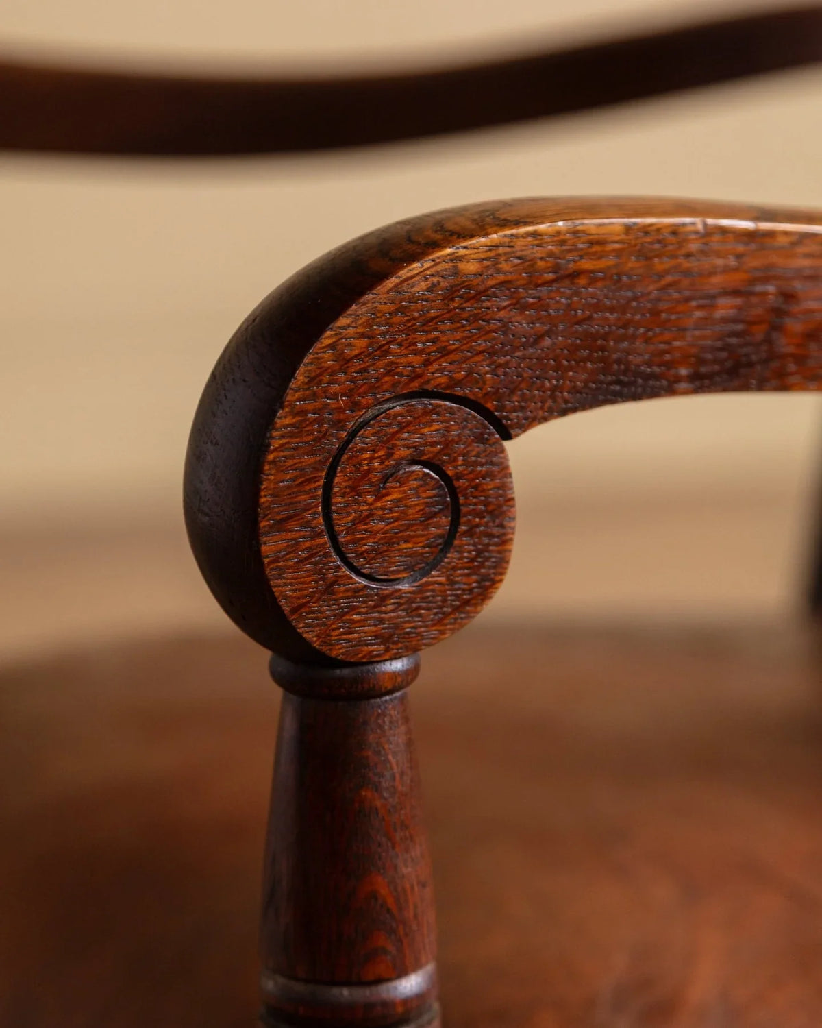 Close-up of carved round wood arm detail on a dark brown leather chair