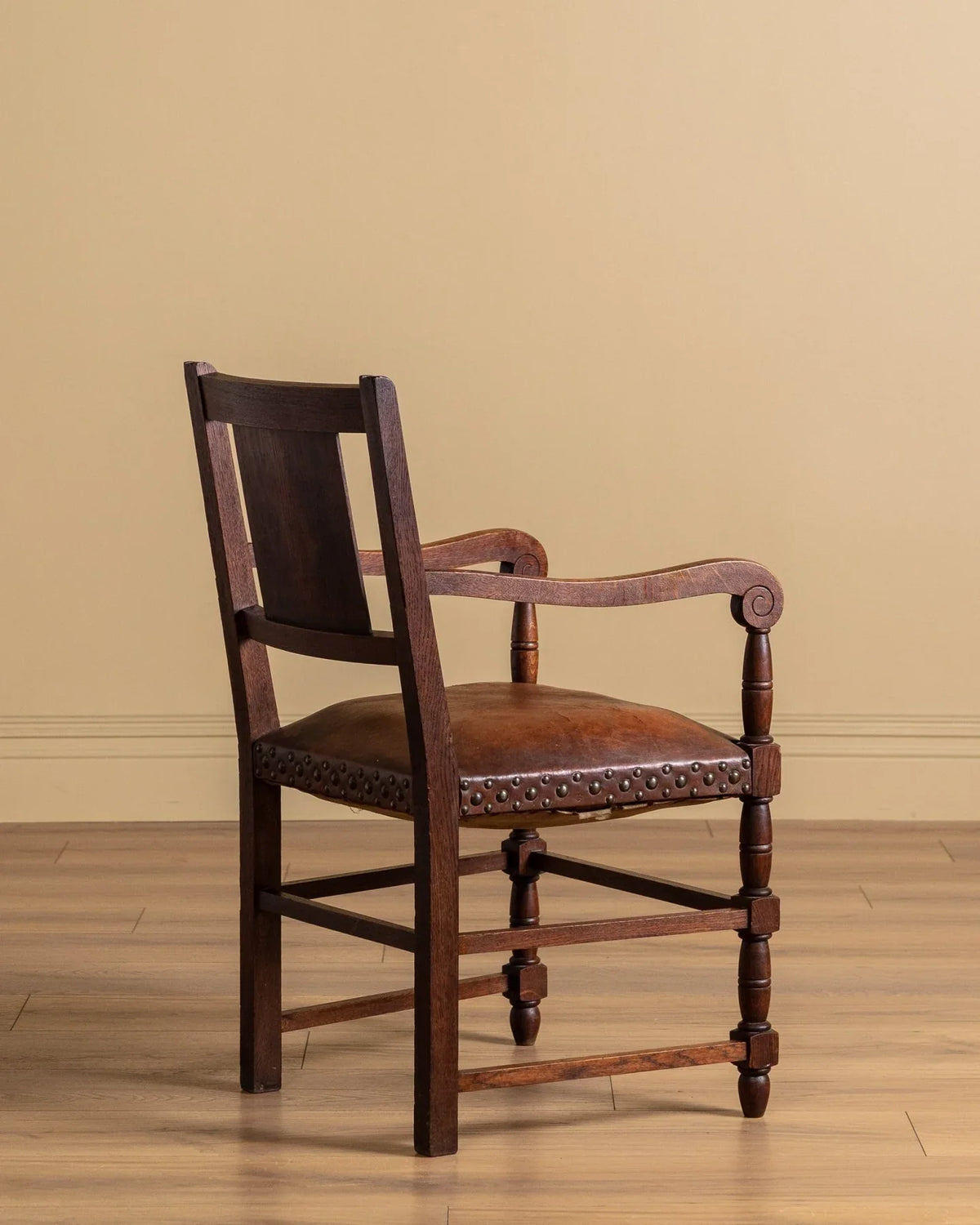 Upholstered armchair with dark wood frame, curved arms, and studded seat edge