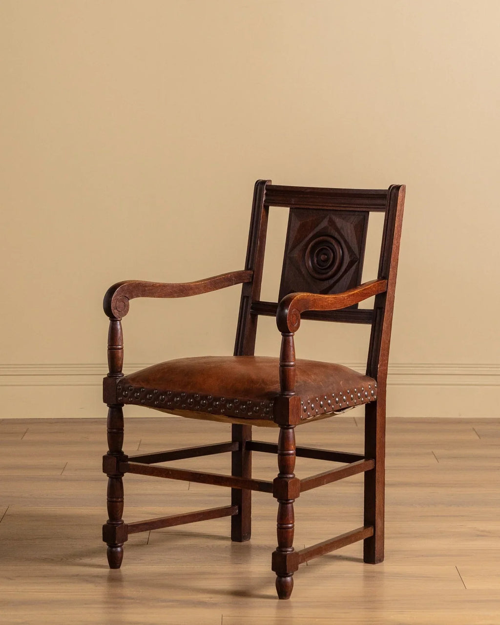 Front view of carved wood open-arm chair with dark brown leather seat and nailhead trim