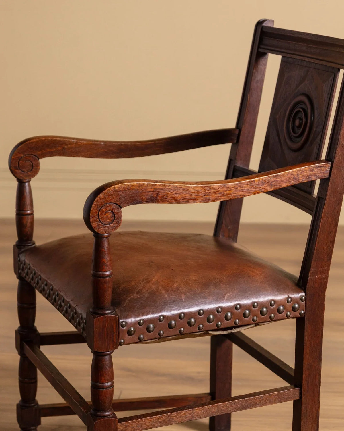 Side view of carved wood open-arm chair with dark brown leather seat and studded trim