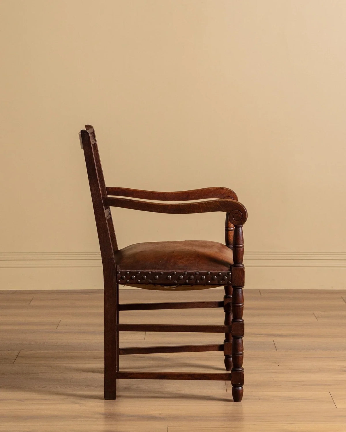 Solid wood armchair with brown cushion, turned legs, and studded trim along seat