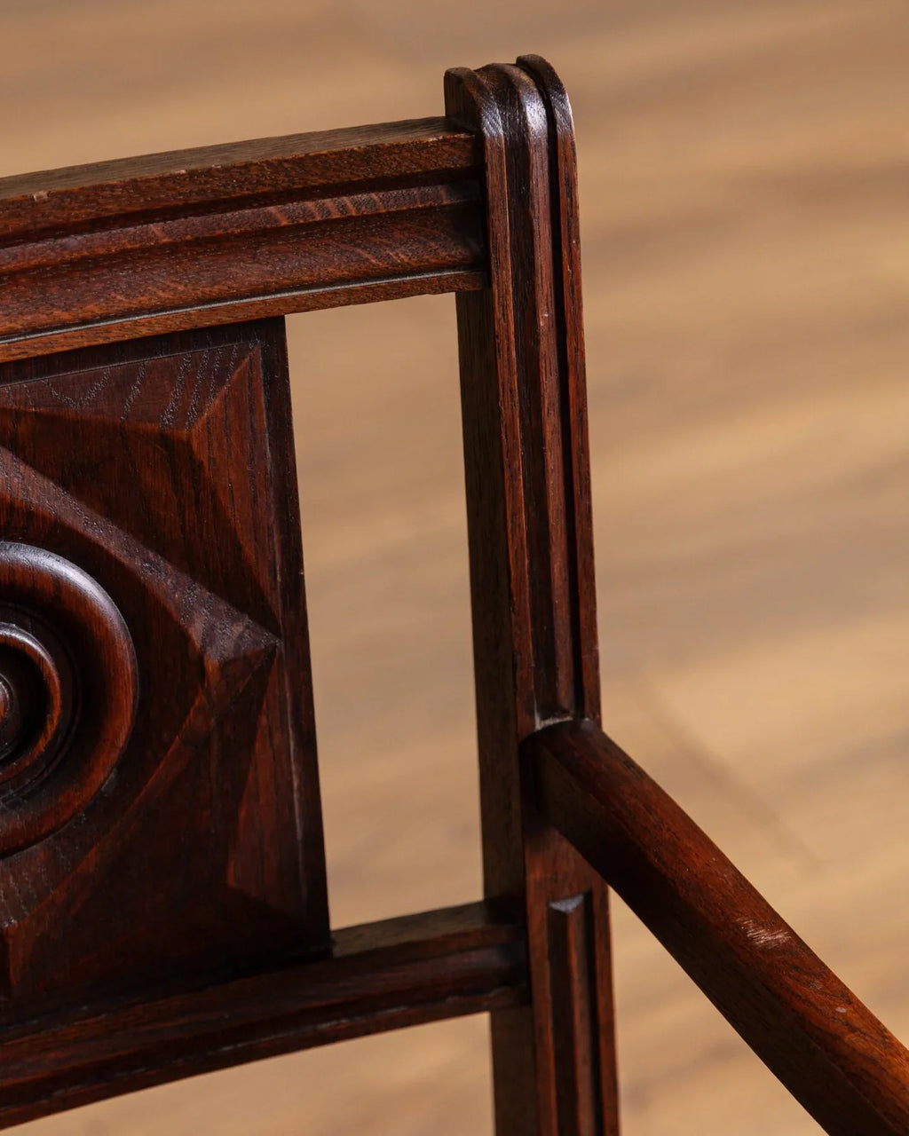 Carved wood side panel and armrest on a dark brown leather open-arm chair