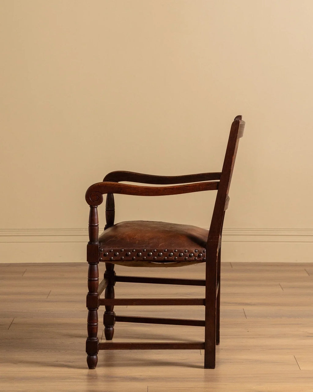 Dark wood open-arm chair with brown upholstered seat and studded trim