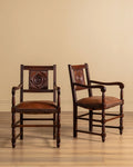 Pair of carved wood open-arm chairs with dark brown leather seats and stud trim