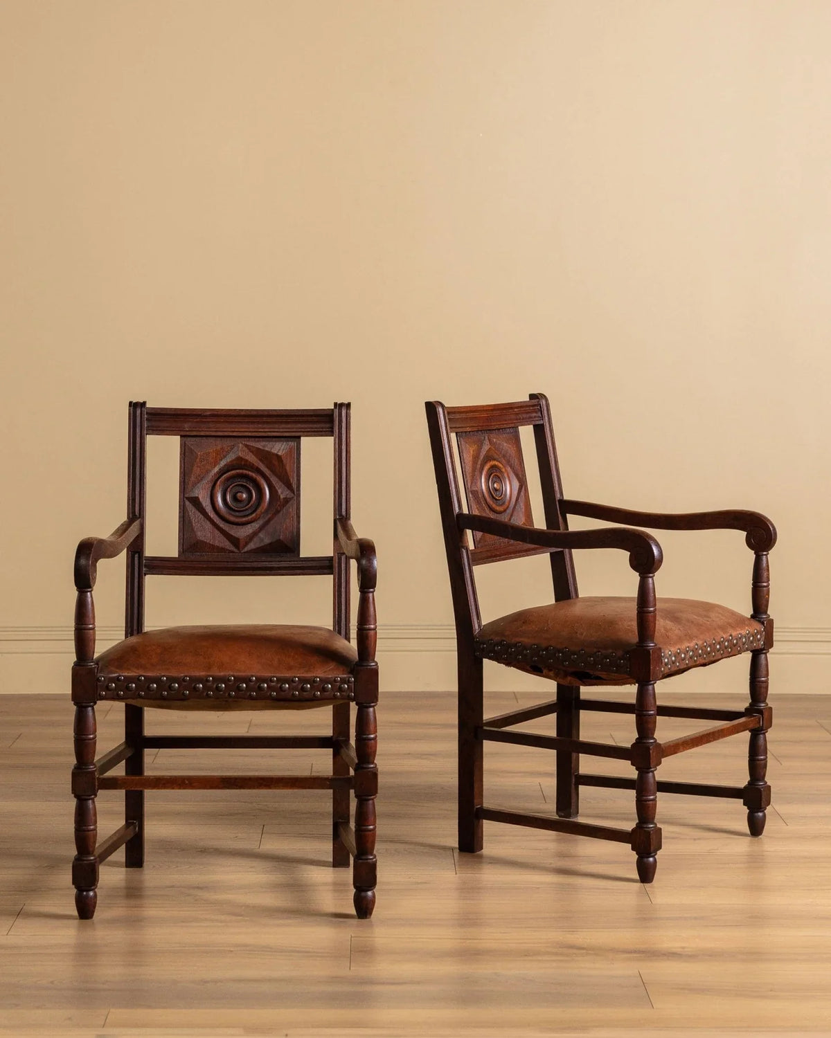 Pair of carved wood open-arm chairs with dark brown leather seats and stud trim