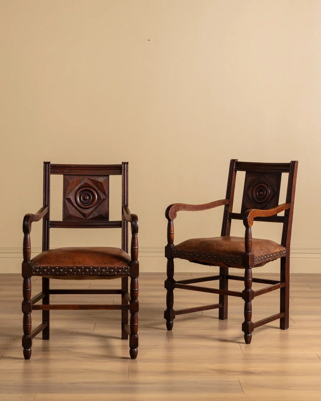 Pair of dark wood armchairs with brown upholstered seats and studded trim