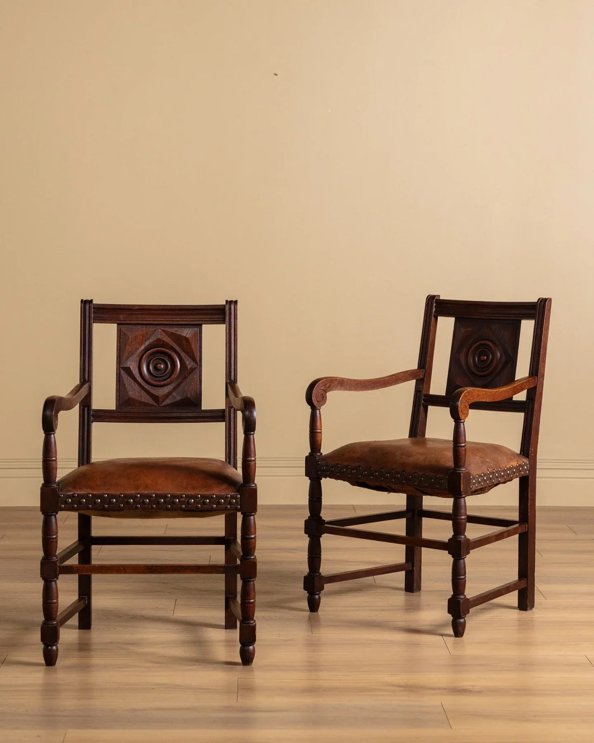 Pair of dark wood armchairs with brown upholstered seats and studded trim