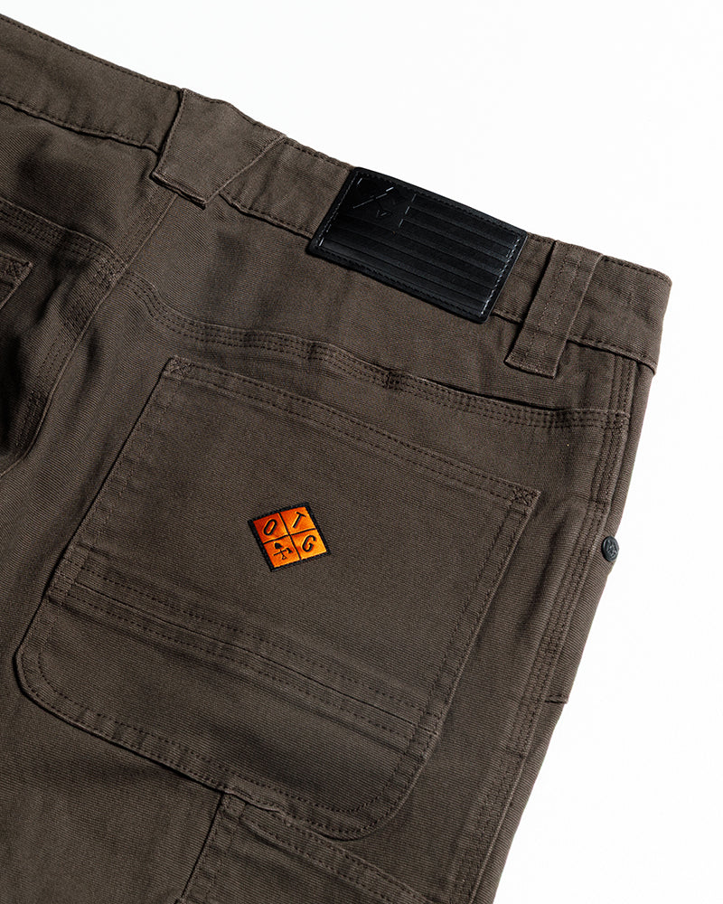 Dark brown cargo pants close-up of front pocket area with logo patch and top flap.