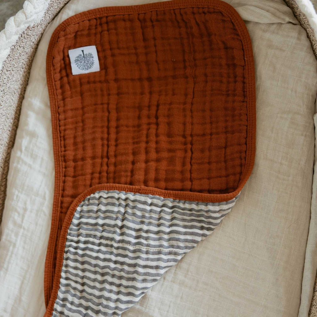 Close-up of rust muslin burp cloth with striped inner panel and patch label