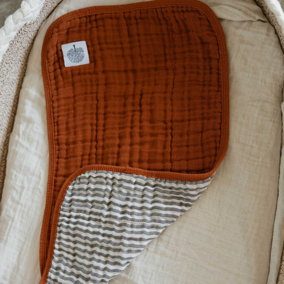 Close-up of rust muslin burp cloth with striped inner panel and patch label