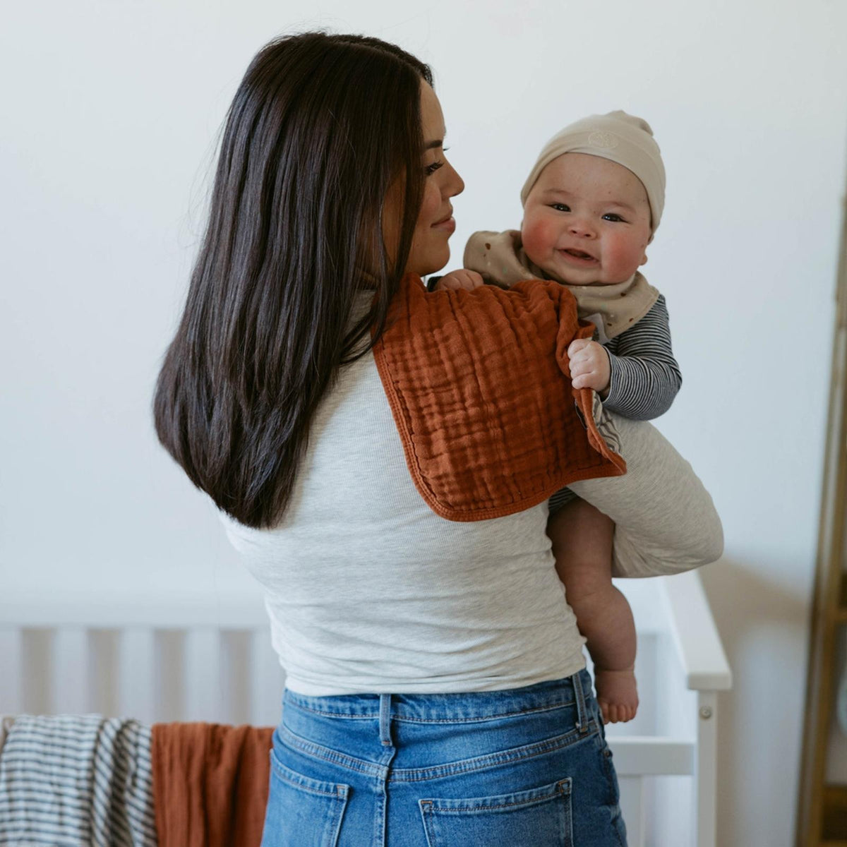 Rust muslin burp cloth held by a parent supporting a baby