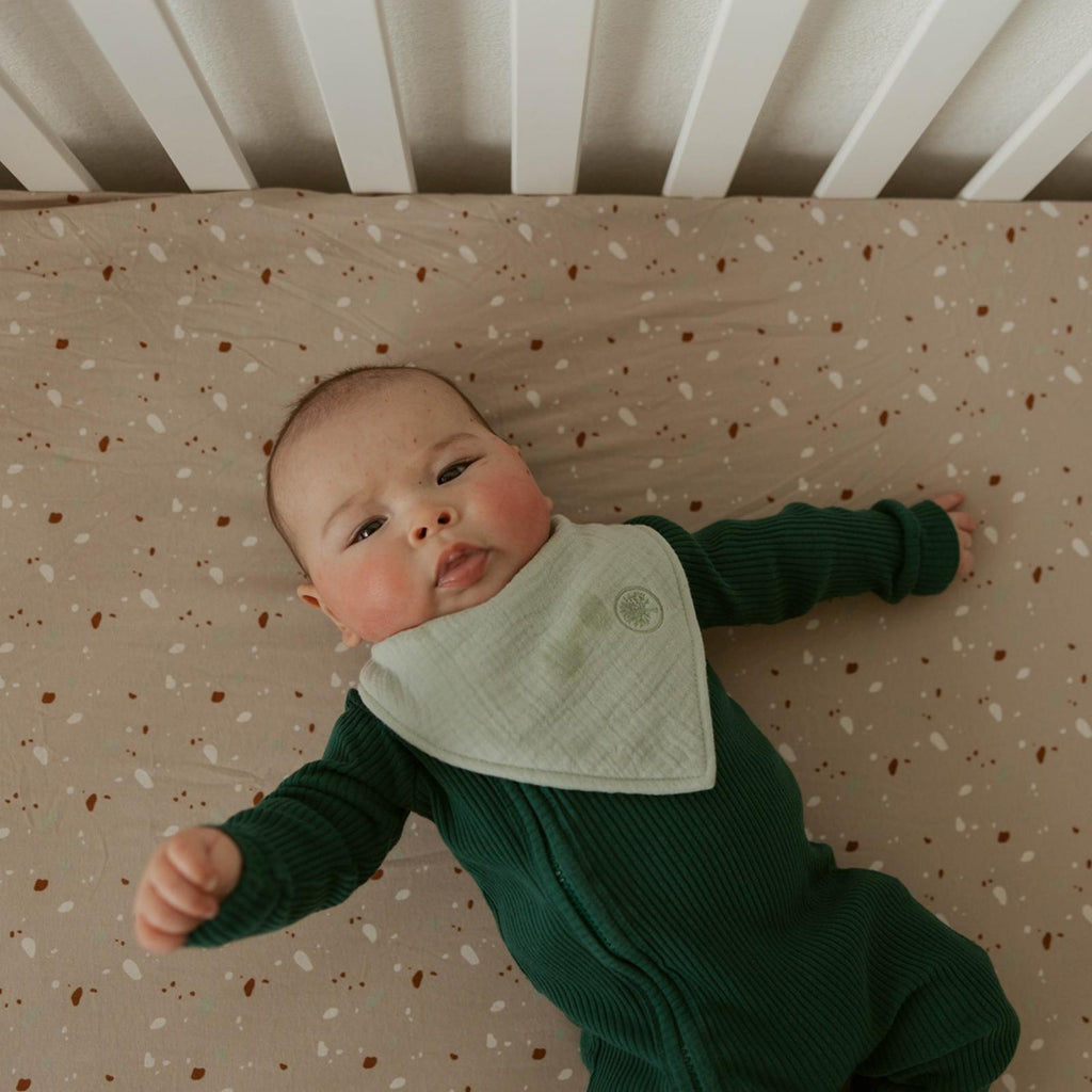 Tan crib sheet with scattered multicolor specks, fitted corner seam visible