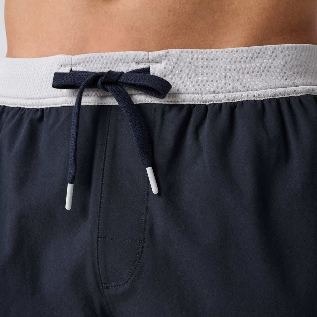 Navy athletic shorts with gray waistband, black drawstring, and side pocket opening.