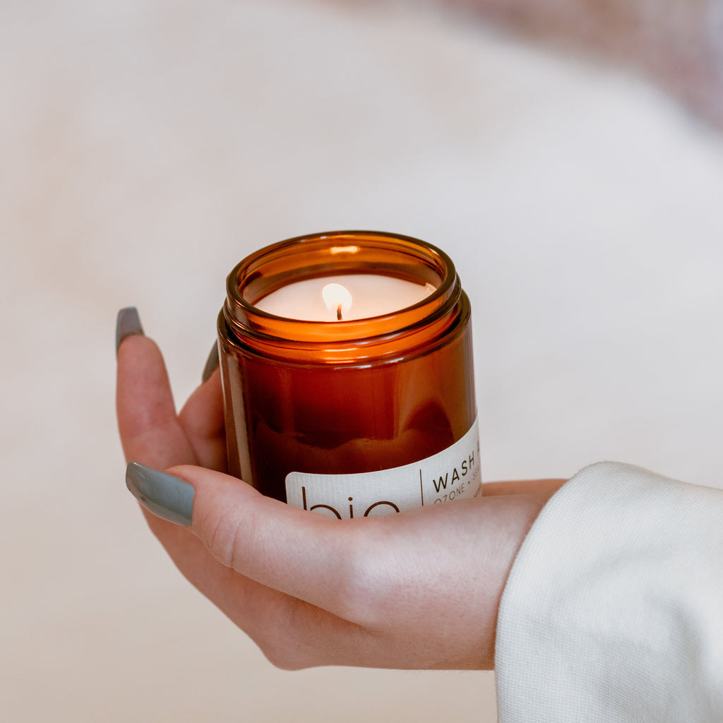 Amber glass candle jar with lit wick, white label on front, held in hand