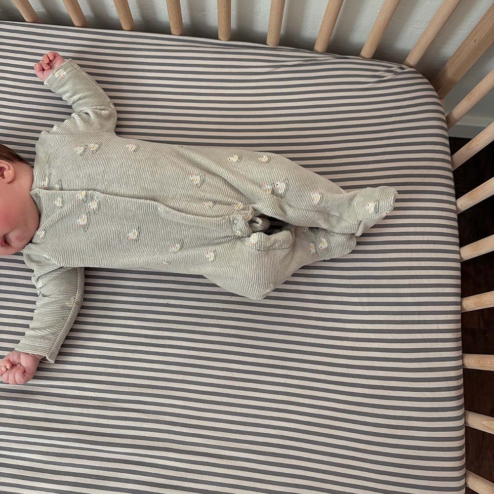 Gray crib sheet with thin white horizontal stripes, laid flat on a crib