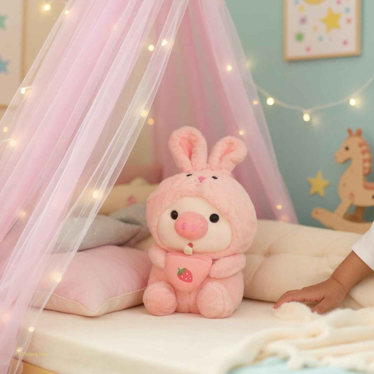 Pink bunny-hood pig boba plush sitting on bed with strawberry drink charm