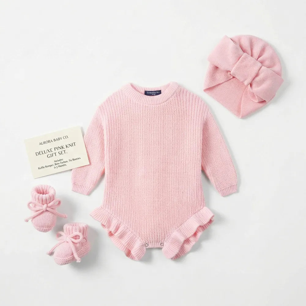 Pink chunky knit baby romper with ruffled hem and snap legs, shown with mini accessories