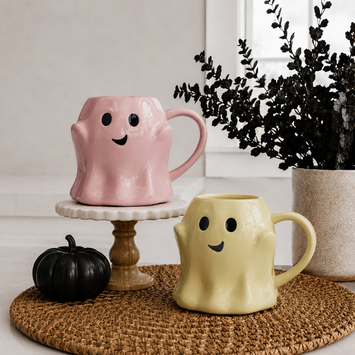 Two ghost-shaped mugs, pink and yellow, each with smiley face