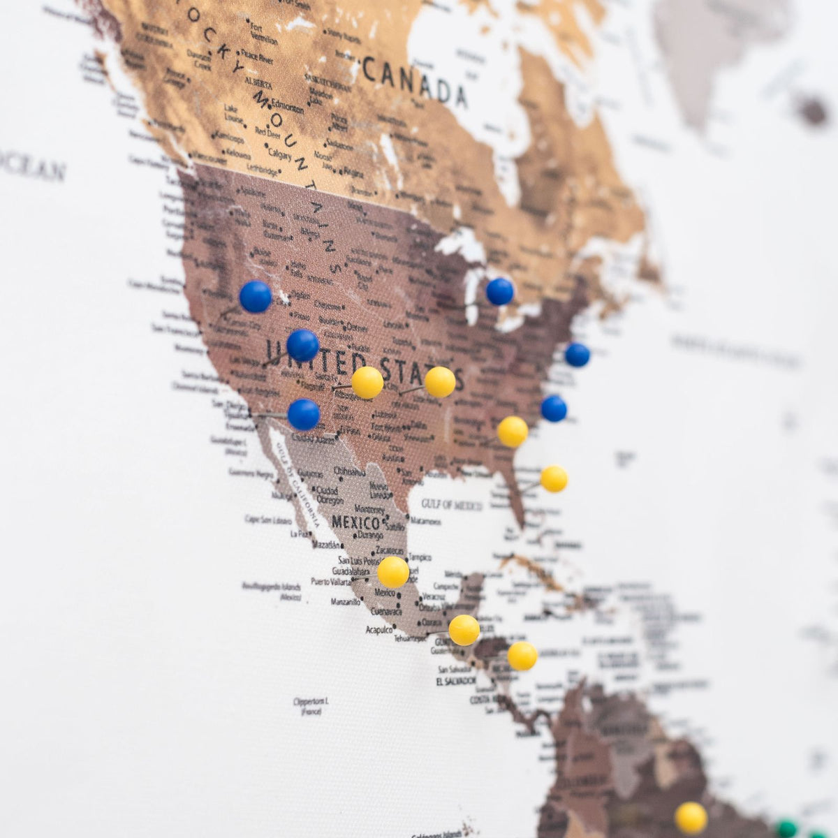 Cluster of blue and yellow push pins on a canvas map of North America