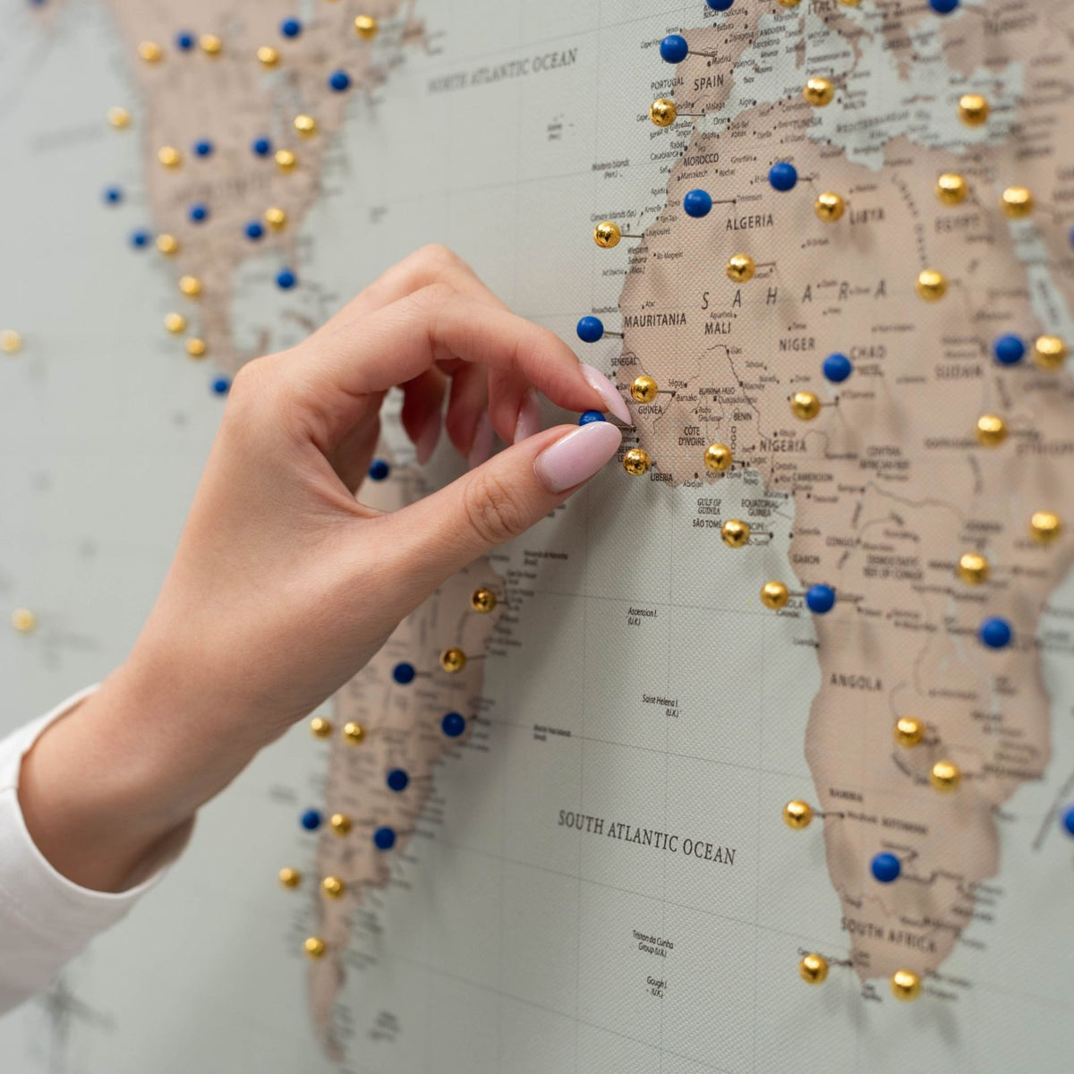 Hand pinning a blue push pin on a canvas world map with gold push pins