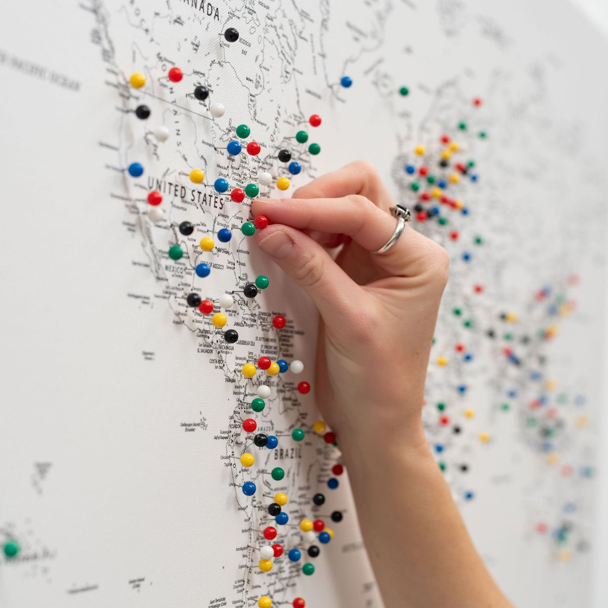 Hand holding green, red, blue, and yellow push pins on a canvas world map