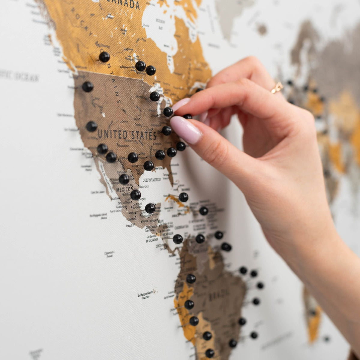 Hand placing black push pins on a canvas map of the United States