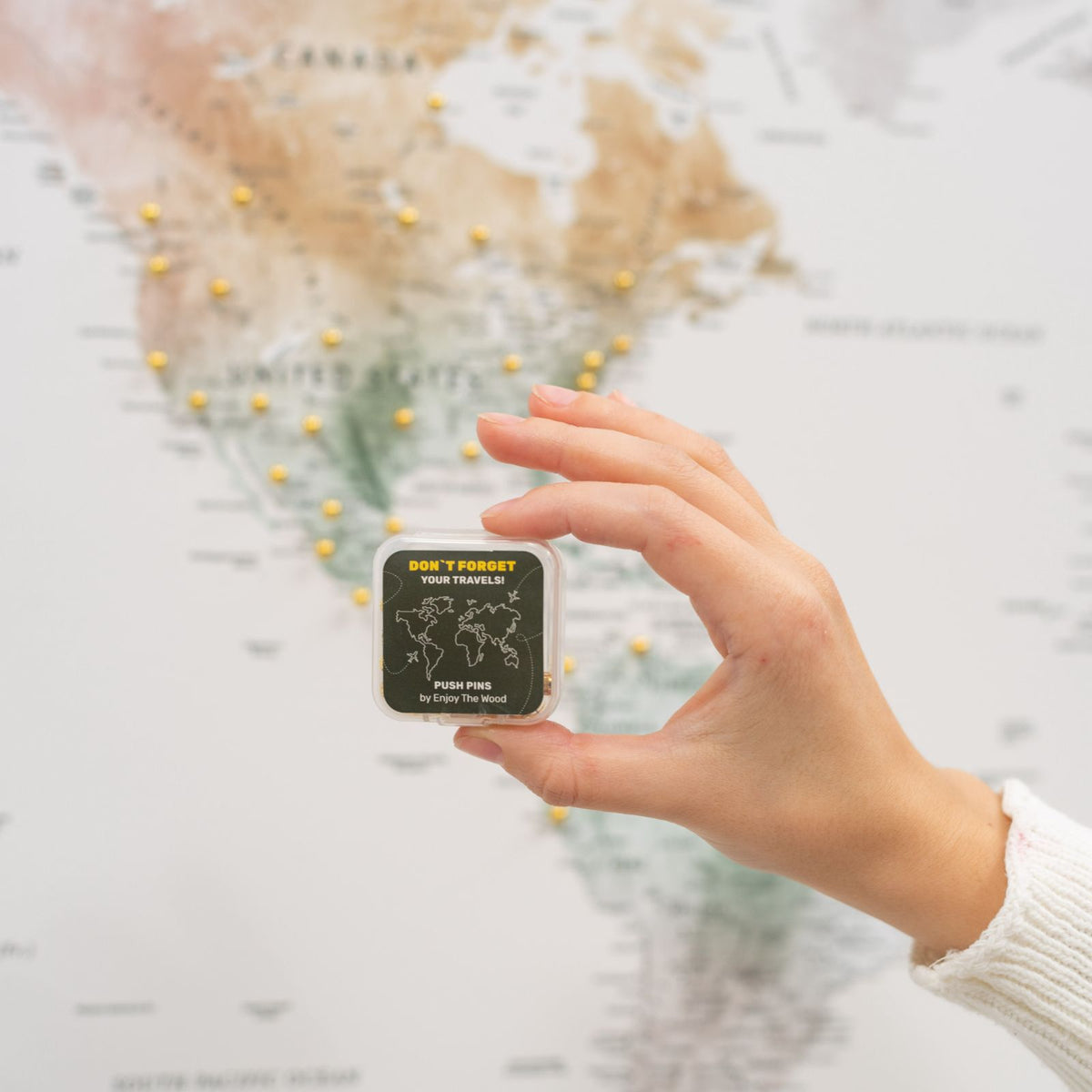 Hand holding push pins through a travel map with a small accessory card