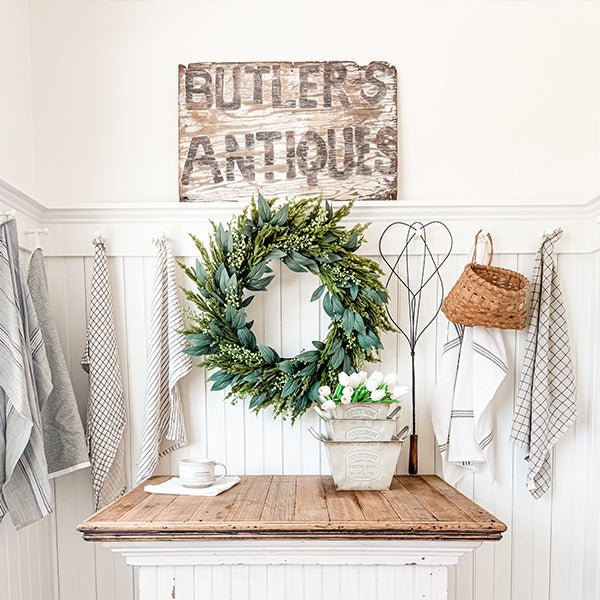 Three distressed white metal planters with handles, arranged on a table with a wreath centerpiece.