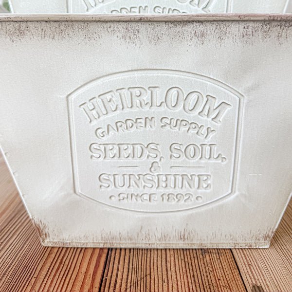 Close-up of a distressed white metal planter with embossed Heirloom garden seal text.