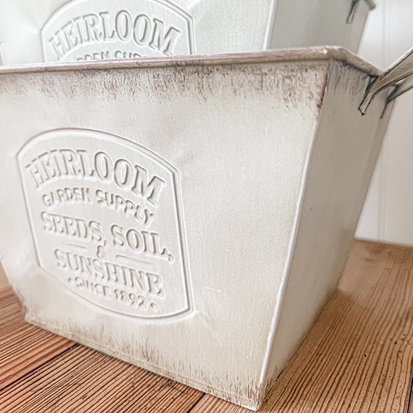 Side view close-up of distressed white metal planter with embossed logo and handles detail.