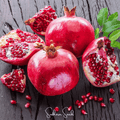 Red pomegranate fruit with arils, cut halves, and loose seeds on dark wood