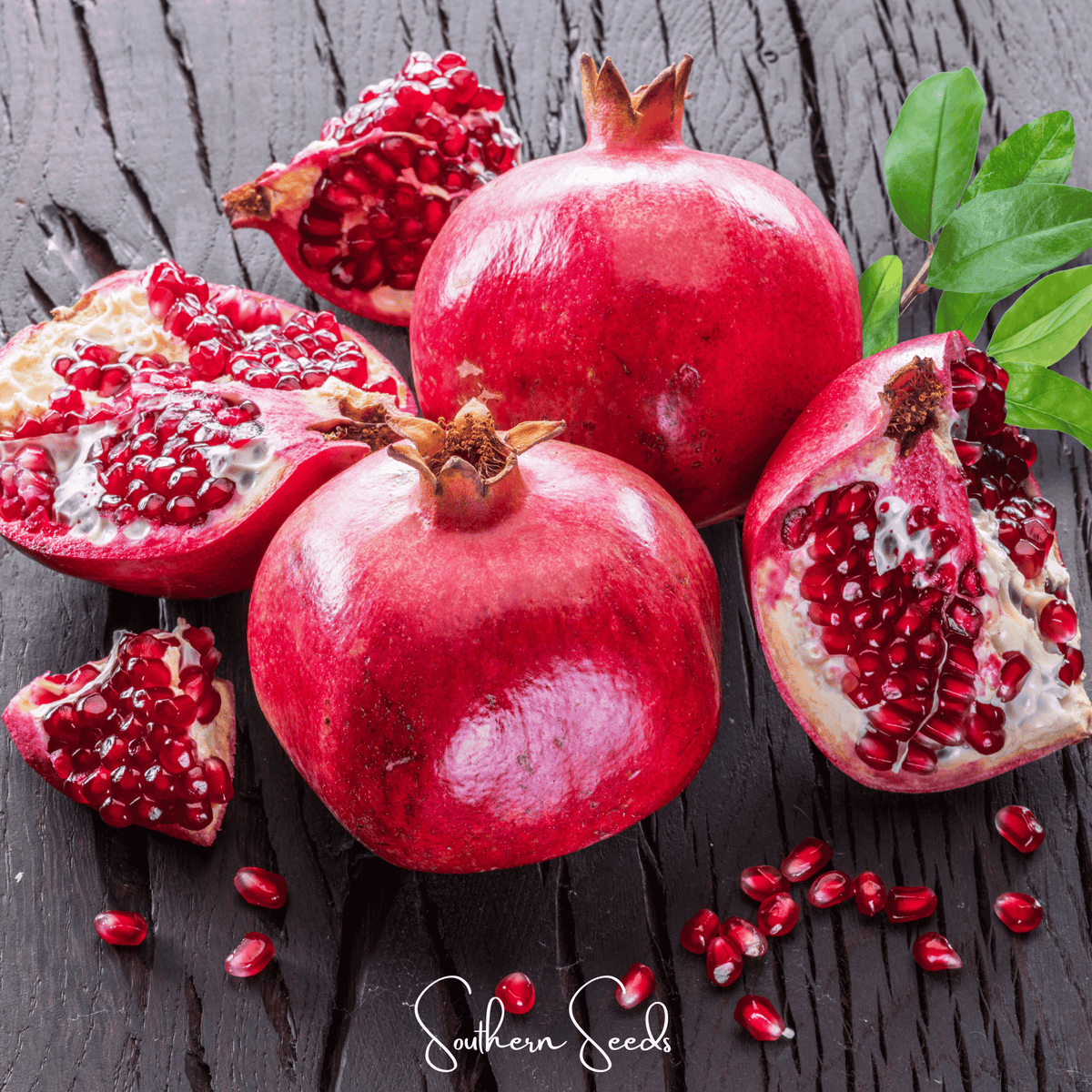 Red pomegranate fruit with arils, cut halves, and loose seeds on dark wood