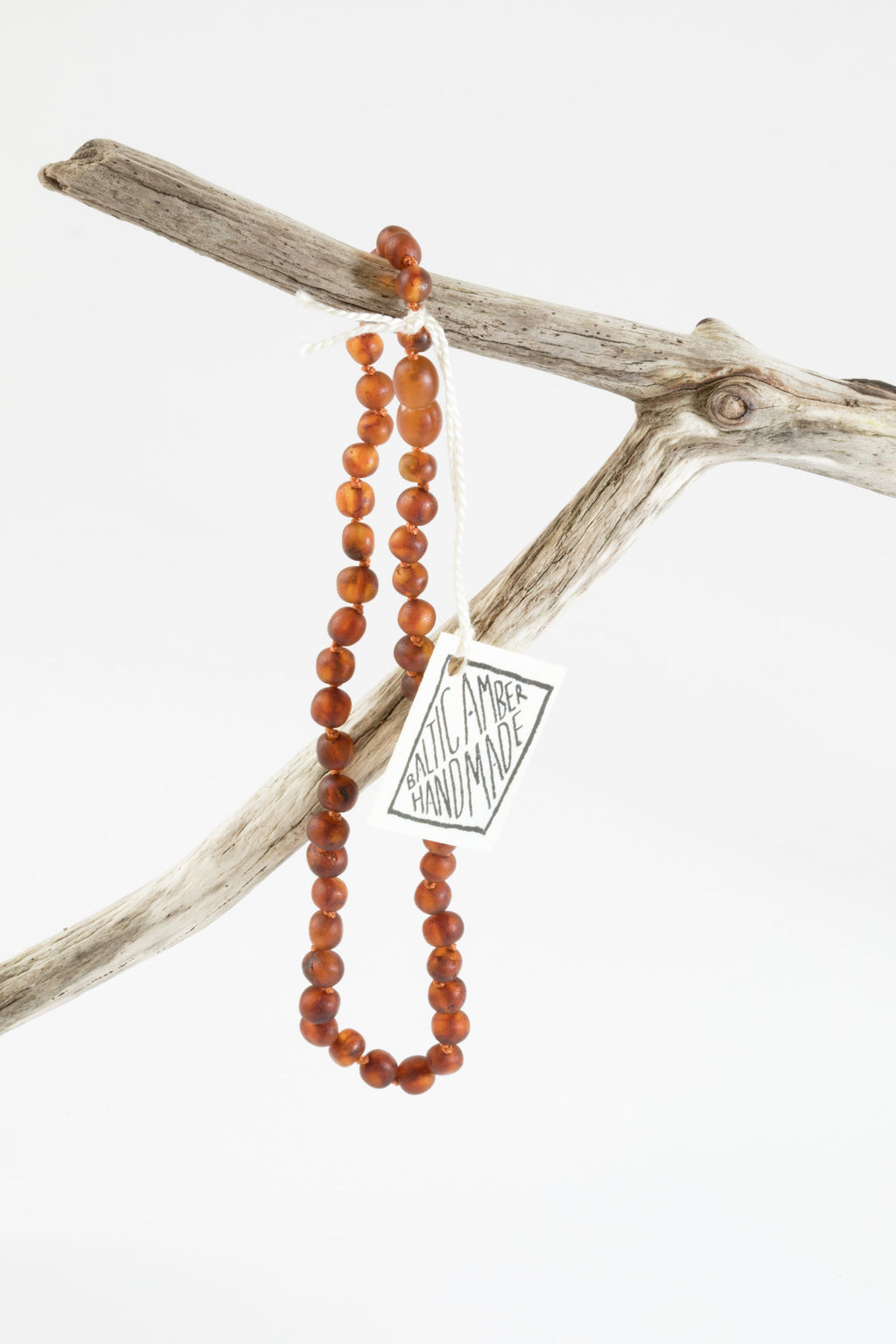 Raw amber bead necklace with round cognac beads, draped on driftwood
