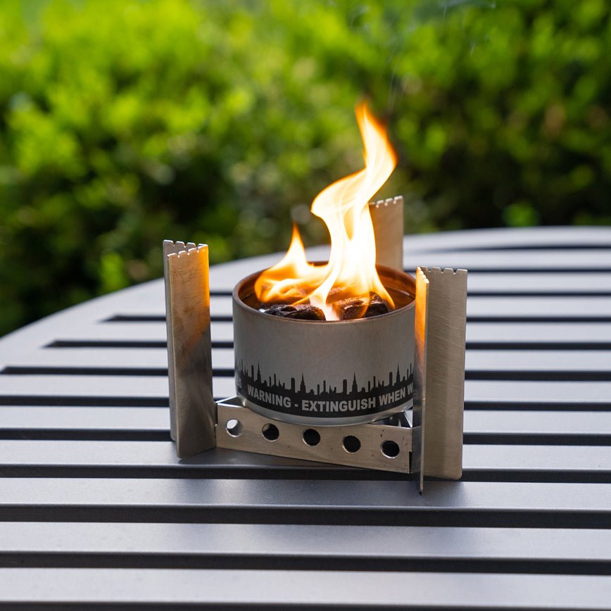 Portable camp stove burner with side panels on outdoor surface, open flame