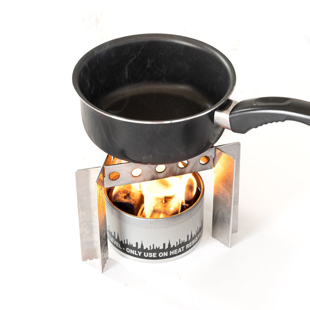 Portable camp stove with black skillet on burner, flames rising