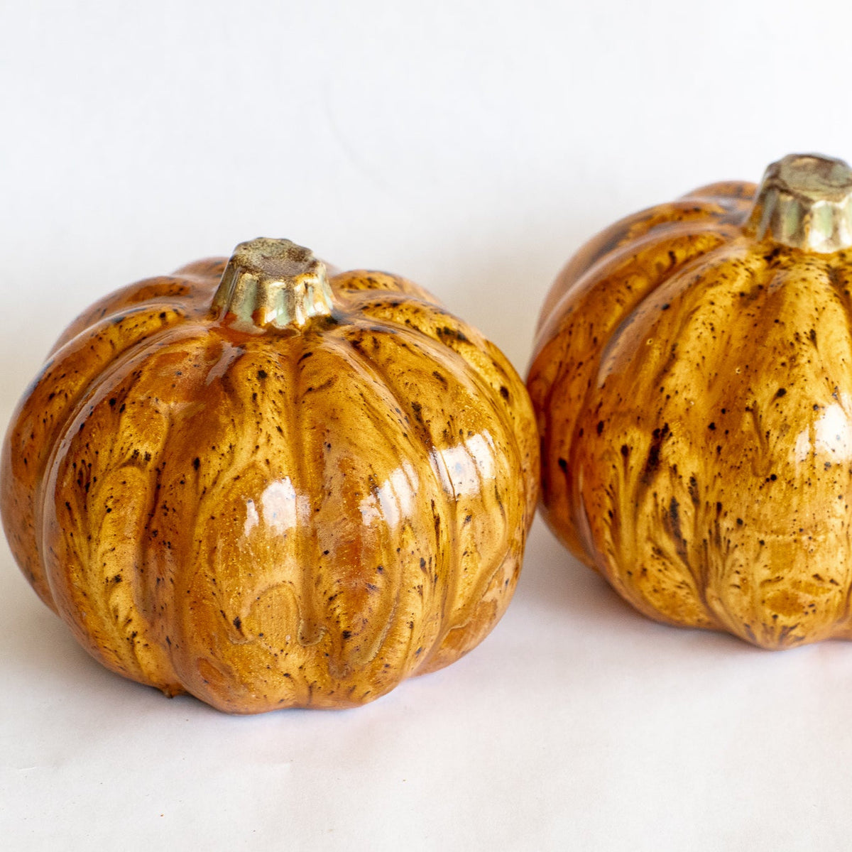 Ceramic pumpkin pair with glossy orange glaze, speckled ribs, and gold-toned stems