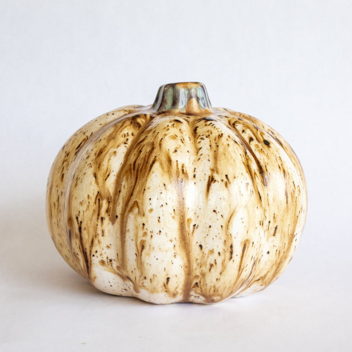 Ceramic pumpkin figurine with beige glaze, dark speckles, and grooved ribbing