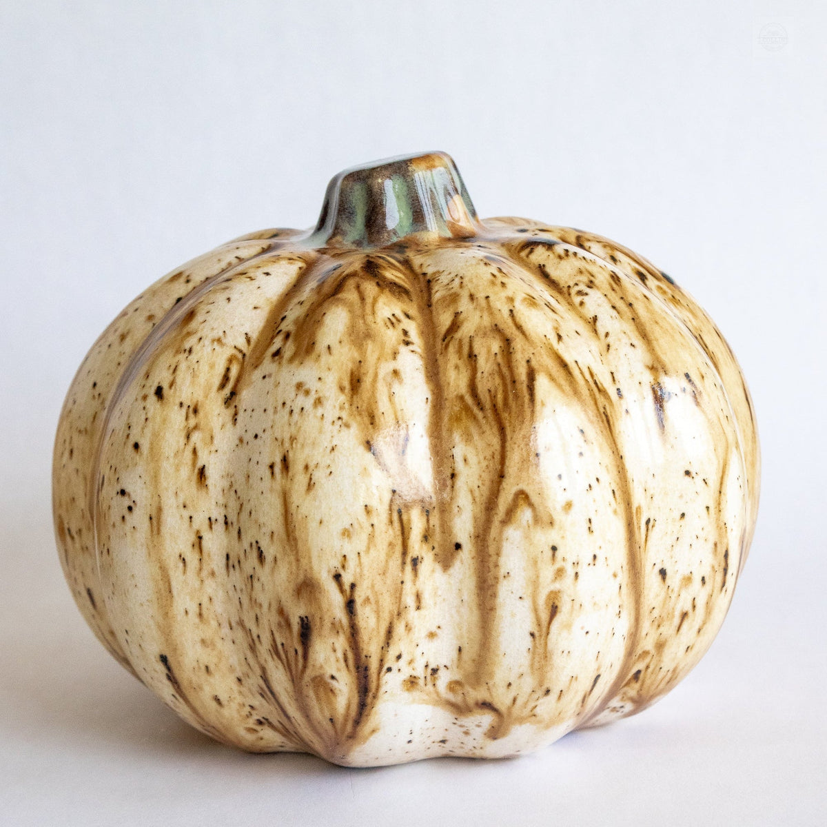 Ceramic pumpkin figurine with beige glaze, dark speckles, and textured ribbing