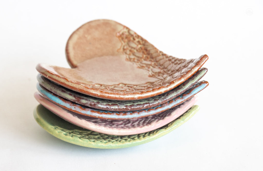 Stack of heart-shaped ring dishes in copper, pink, and green glazes with textured pattern