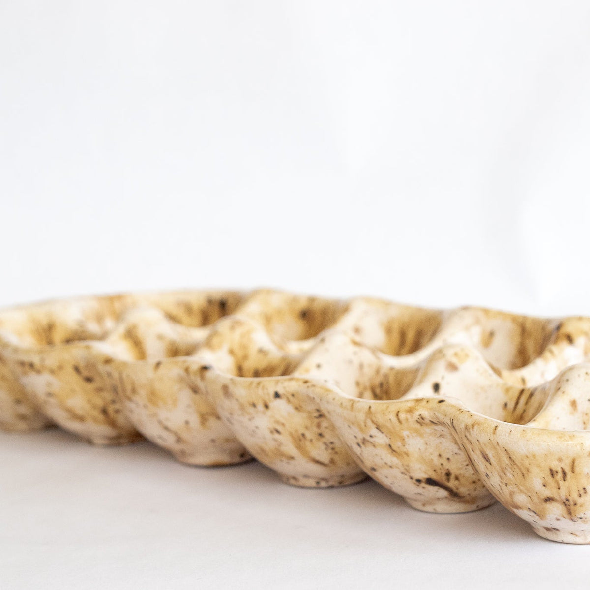 Ceramic egg carton with row of speckled egg cups, beige glaze with brown flecks