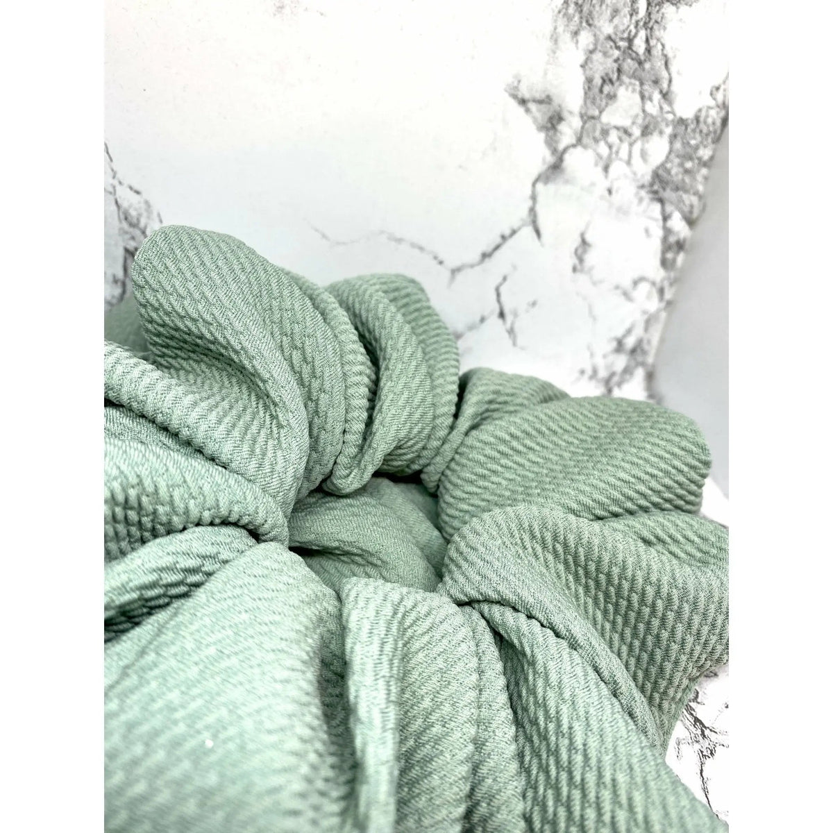 Close-up of sage green scrunchie knot with ribbed texture and pleats
