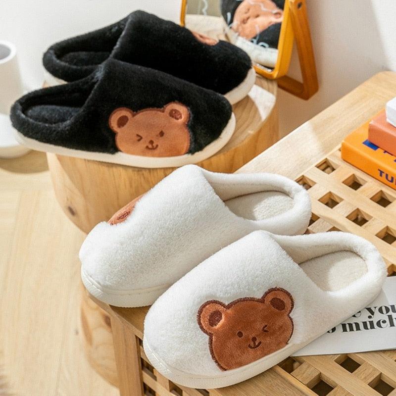 Fuzzy house slippers with bear patch, white pair in front and black pair behind