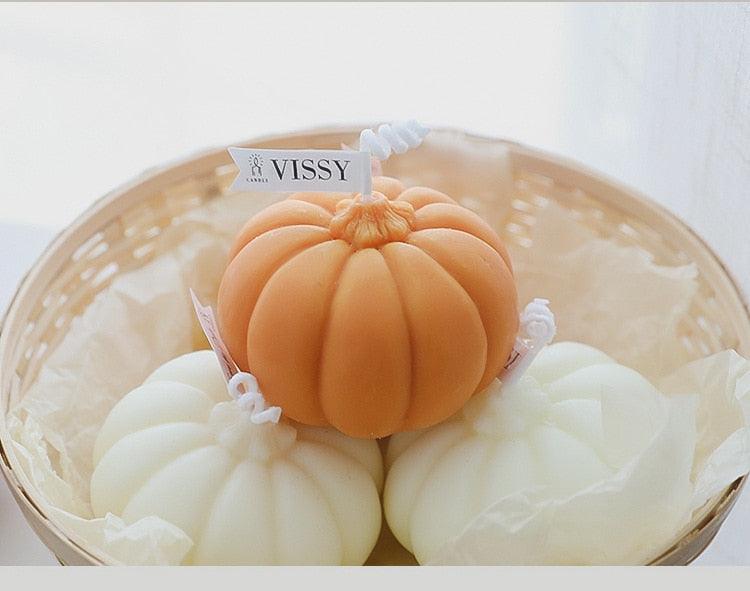 Orange pumpkin-shaped candle with white pumpkin and label on top of a tray