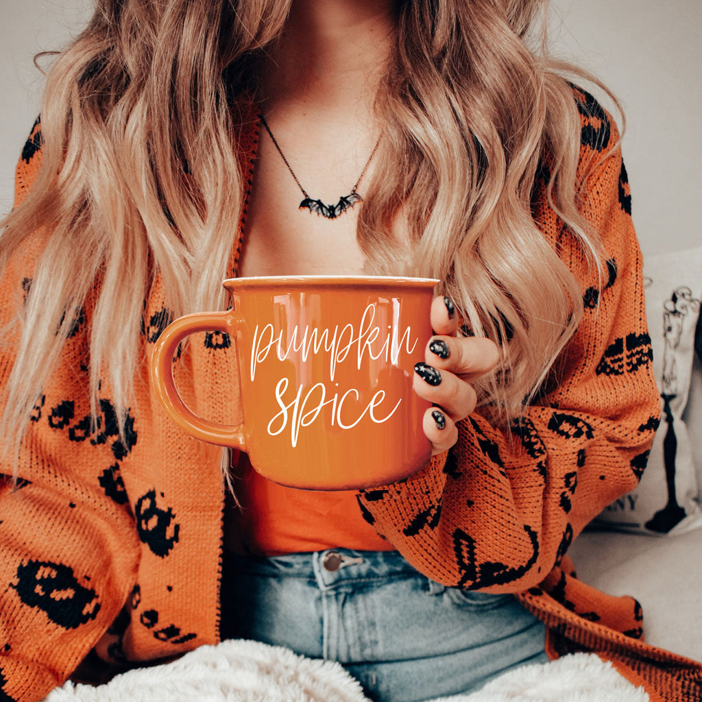 Orange mug held to chest, Pumpkin Spice script lettering on front