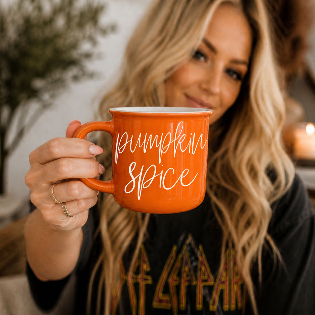 Orange ceramic mug with white “pumpkin spice” lettering held by person