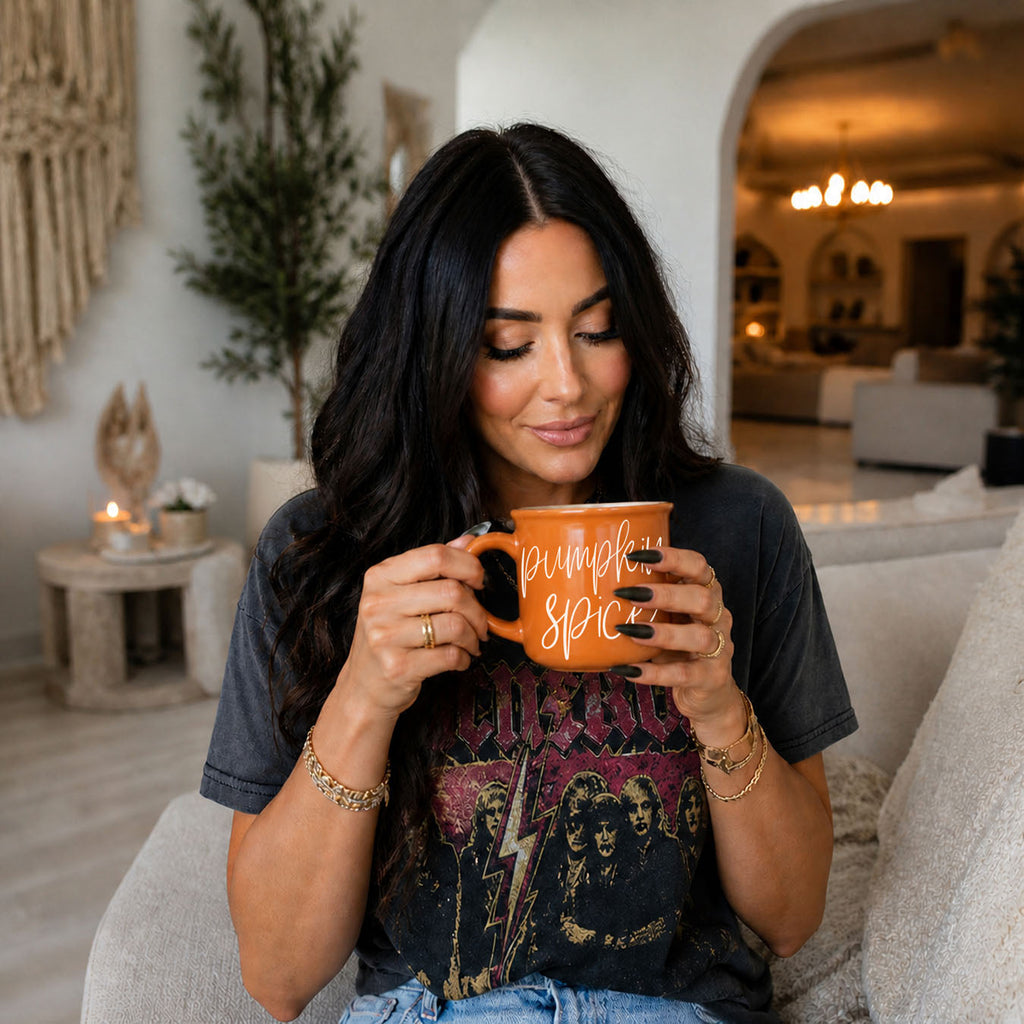 Orange ceramic mug with white “pumpkin spice” lettering in person’s hands