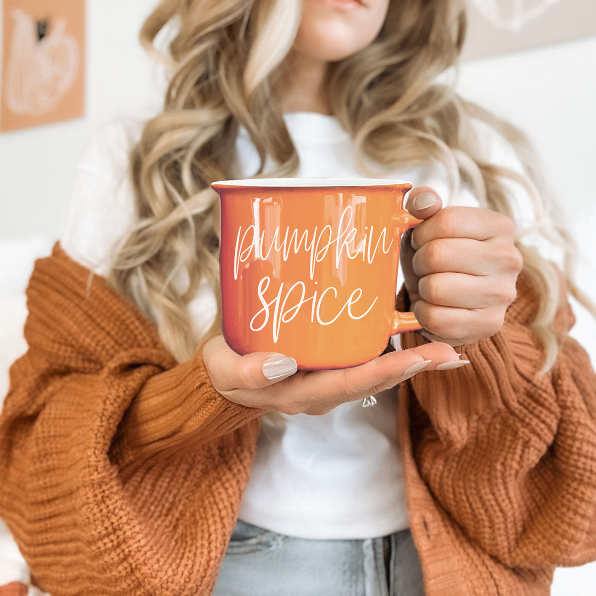 Orange ceramic mug with white “pumpkin spice” lettering held near chest
