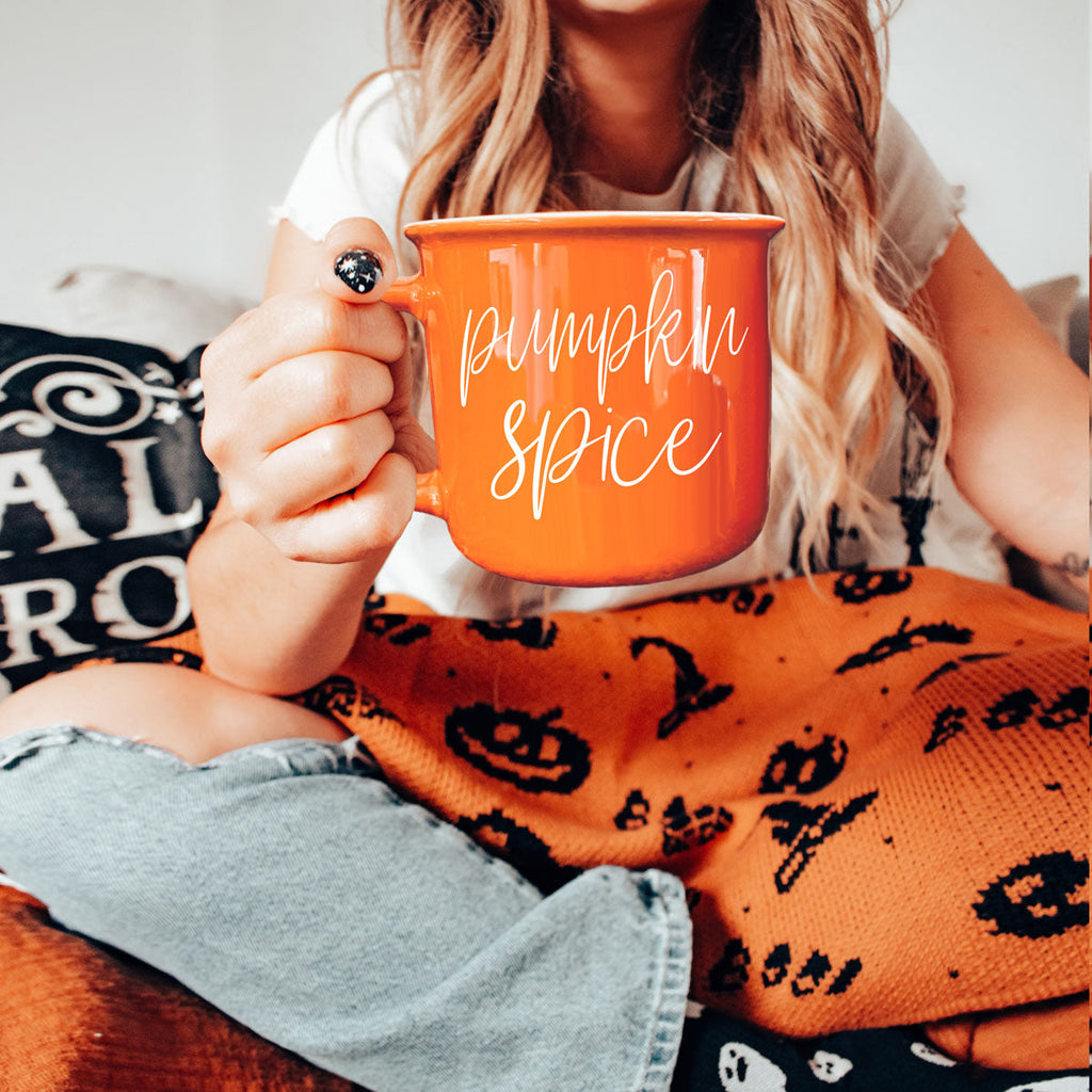 Orange ceramic mug with 'Pumpkin Spice' text, held in lap