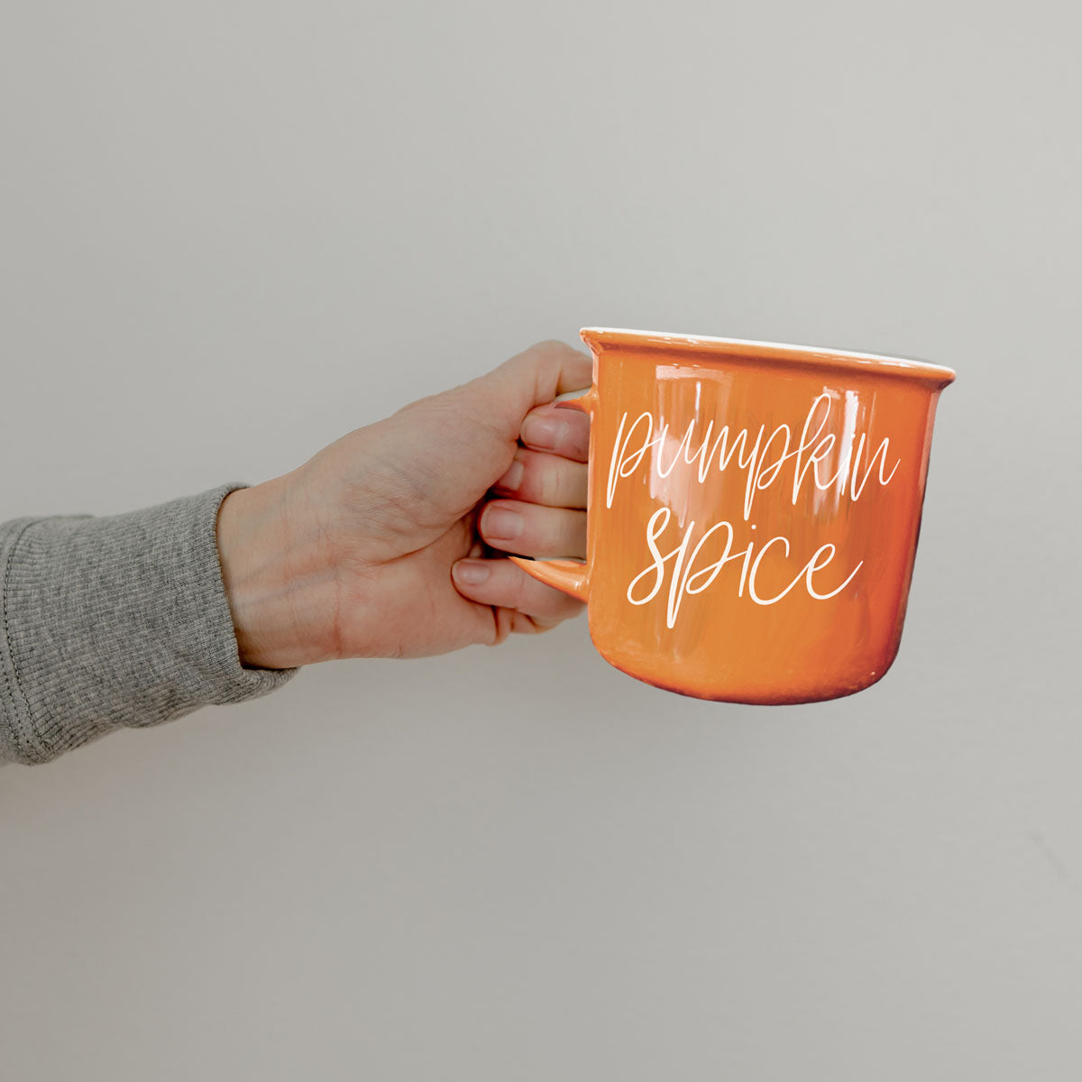 Orange ceramic mug with 'Pumpkin Spice' lettering, held by gray sleeve