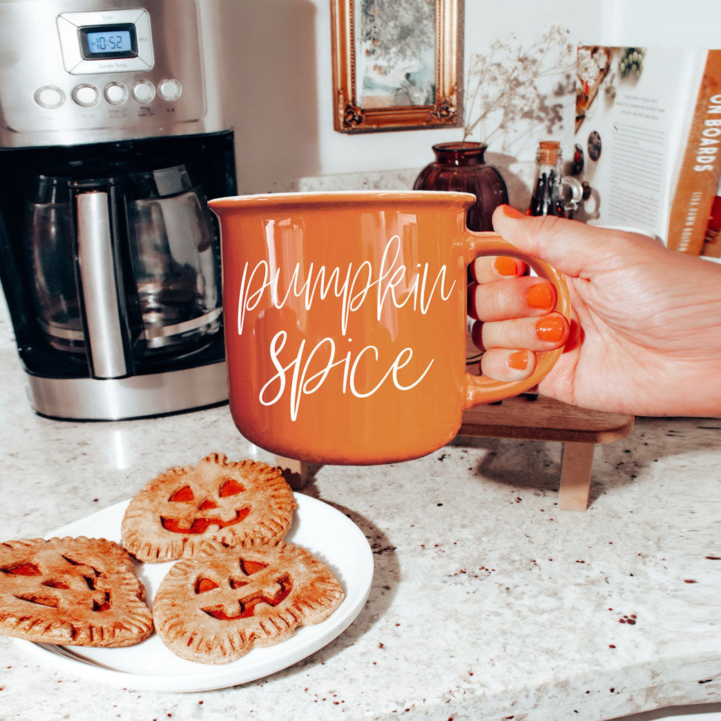Orange mug with “Pumpkin Spice” script text held near kitchen counter